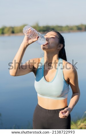 Asian women drink water after jogging, play sports with clear plastic bottles, and smile at you in the park.