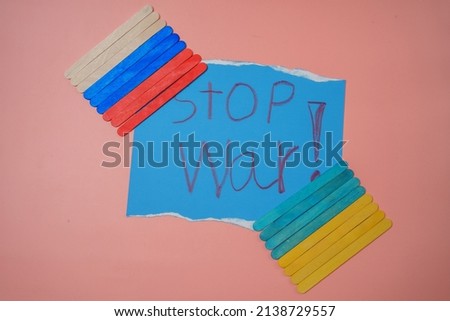 Small wooden pieces arranged in a row depicting the Russian and Ukrainian flags with the text stop war in the center against a pink background. No war, stop war, russian aggression.