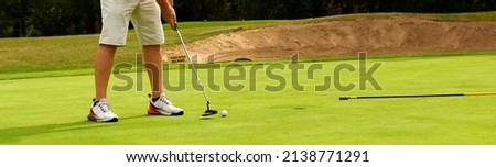 Golfer on the green with a putter in his hands. A player on the green evaluates the slopes and distance from the hole before aiming the ball towards the flag.