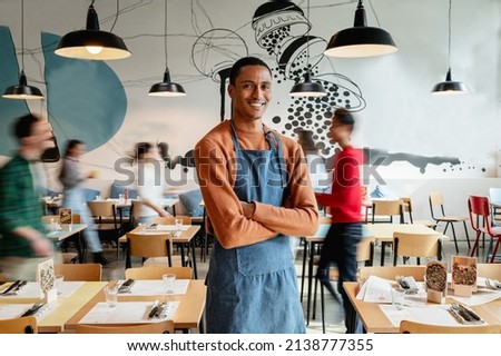 portrait of smiling male owner or waiter in cafe with unrecognizable blurred employes moving.