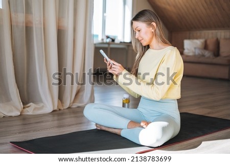 Young adult fitness blonde woman practice morning yoga using mobile phone near window of home