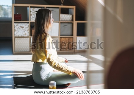 Young slim fitness blonde woman practice morning yoga near the window of home