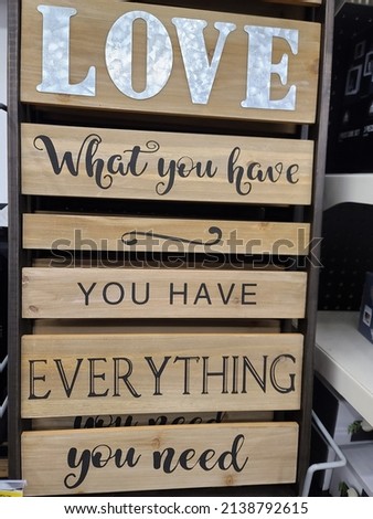A closeup of a wooden sign hanging on a shelf. It reads "LOVE WHAT YOU HAVE YOU HAVE EVERYTHING YOU NEED".