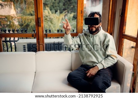 Bearded young man wearing VR glasses and pointing to the camera. Entertainment at home concept