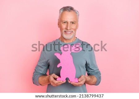 Photo of dreamy funny man pensioner dressed grey shirt holding rabbit isolated pink color background