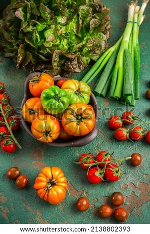 Assortment of tomatoes, lettuce and sprin onions on green background