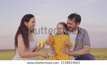 mother father little child blow bubbles picnic park. happy family life. concept children's dream. kid laughs with parents in nature. girl daughter plays a game with mom and dad inflating soap bubbles