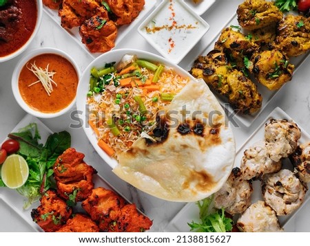 Assorted famous indian and pakistani food table vegetable biryani, Butter Chicken, paneer Chicken Tikka boti kebab, lime, Kali Mirchi, tomato sauce, raita, roti, salad, top view on grey background Royalty-Free Stock Photo #2138815627