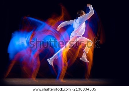 High jumps. Young man in sports white suit dancing hip-hop isolated on dark background in mixed neon light. Youth culture, hip-hop, movement, style and fashion, action. Modern street dancing style Royalty-Free Stock Photo #2138834505