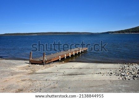 Rustic, wooden dock extends out into Lake Norfork, in Northern Arkansas.  Boat access is on either side.  Lake water shows blue along with the clear sky. Royalty-Free Stock Photo #2138844955