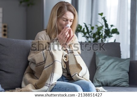 The sick woman is sitting on the couch at home, has a cough and fever, cold and runny nose Royalty-Free Stock Photo #2138851427