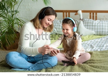 mom and daughter listen to music in headphones from their smartphone. family having fun together.