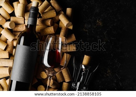 Festive composition. A bottle of red wine, a corkscrew and a wine glass lie on wine corks on a black background. There is free space to insert. Holiday, celebration, date, romantic evening. Banner. Royalty-Free Stock Photo #2138858105