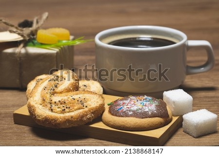 Poppy seed cookies, chocolate covered cookies and sweet sprinkles, a cup of black coffee and a gift box on the table