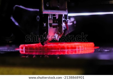 Automatic three dimensional printer machine printing red flat plastic model at modern technology exhibition - close up. 3D printing, futuristic, prototype, manufacturing and production concept Royalty-Free Stock Photo #2138868901