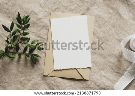 Blank paper card mockup, envelope, green branch, silk ribbon on linen tablecloth. Wedding invitation card design, greeting card template. Royalty-Free Stock Photo #2138871793