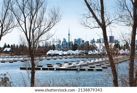 The Toronto skyline in between trees during spring in Toronto, Ontario, Canada. A blue sky and boat docking stations can be seen in the background.