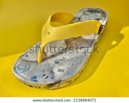 Broken and wasted yellow children flip flops on yellow horizontal studio background