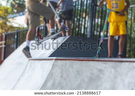 Skate park view with kids on a kick scooter doing tricks and stunts, boys in a skate park riding bmx bike and skate, playing and enjoying summer on new ramp, teenagers skateboarders and bmx riders 