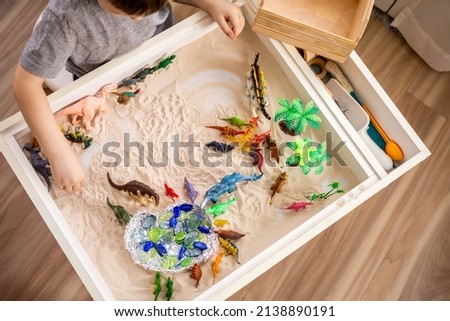 Top view cute little baby boy playing sensory box dinosaur world with kinetic sand table enjoy happy childhood. Male kid use carnivorous and herbivorous dinosaurs early development Montessori material Royalty-Free Stock Photo #2138890191