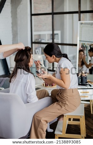 Woman makeup artist and hairdresser getting ready female to event wedding or important meeting. Group of feminine friends preparing cosmetic beauty care hair face procedure at home bedroom interior Royalty-Free Stock Photo #2138893085