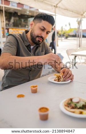 Young Hispanic man enjoying a carnitas taco outside