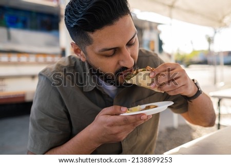Young Hispanic man enjoying a carnitas taco outside