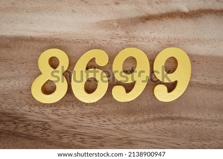 Wooden  numerals 8699 painted in gold on a dark brown and white patterned plank background.