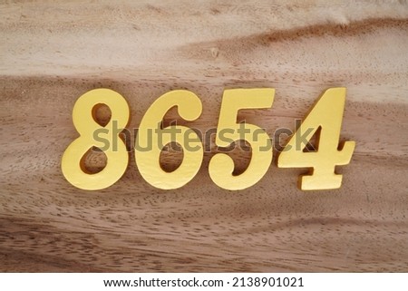 Wooden  numerals 8654 painted in gold on a dark brown and white patterned plank background.