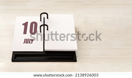 july 10. 10th day of month, calendar date. Stand for desktop calendar on beige wooden background. Concept of day of year, time planner, summer month.