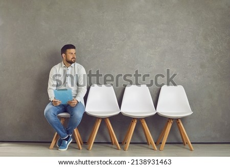 Worried young caucasian male job seeker vacancy candidate holding resume form waiting for interview meeting sitting on chair looking aside. Jobless applicant at recruitment staffing agency Royalty-Free Stock Photo #2138931463