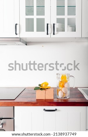 White kitchen with glass jug filled with eggs. Happy Easter card with gift box and eggs.