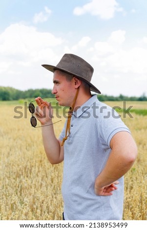 Businessman harvester. Portrait of farmer standing in gold wheat field with blue sky in background. Young man wearing sunglasses and cowboy hat in a field examining wheat crop. Oats grain production.
