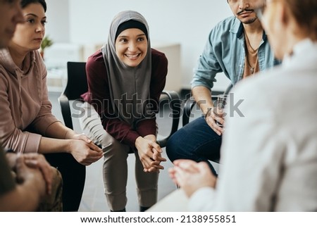 Group of diverse people having group meeting with their therapist at mental health center. Focus is on happy Muslim woman.