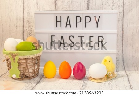 Stylish lightbox text frame with happy easter inscription. Pink, blue, white and yellow eggs in a basket, chick yellow easter symbol .Colorful easter eggs. 
