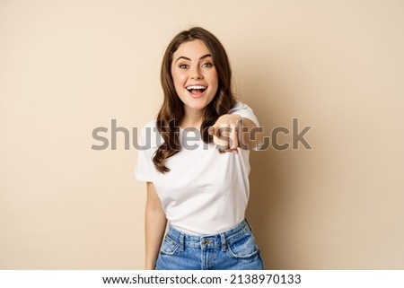 Its you, congrats. Smiling beautiful woman pointing finger at camera, congratulating, praising you, standing over beige background