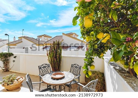 Cute terrace patio with empty table and chairs and blooming lemon tree, rooftops view of residential neighbourhood houses against blue sky during sunny summer day. Summer vacation concept. Spain