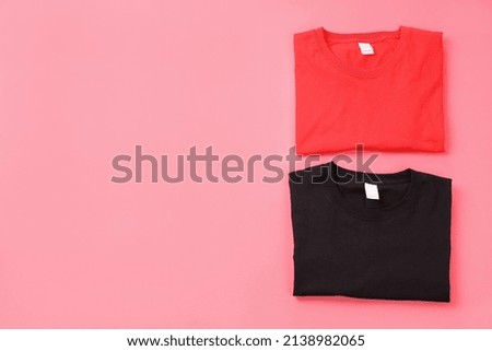 Folded black and red t-shirts on pink background