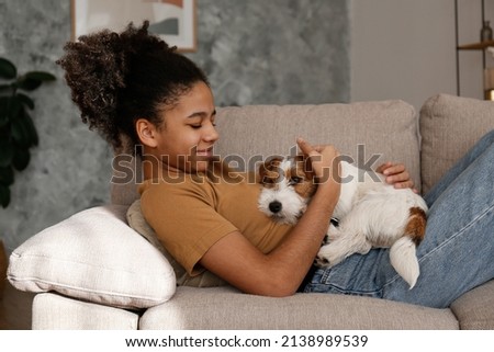 Portrait of young beautiful teenage girl with her adorable wire haired Jack Russel terrier puppy at home. Teenager with rough coated pup sitting on the couch. Interior background, close up, copy space Royalty-Free Stock Photo #2138989539