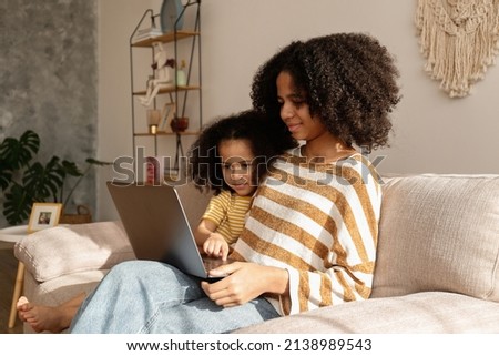 Two beautiful black girls of different age on a video call at home. Loving sisters sitting together on the couch with laptop. Background, close up, copy space.