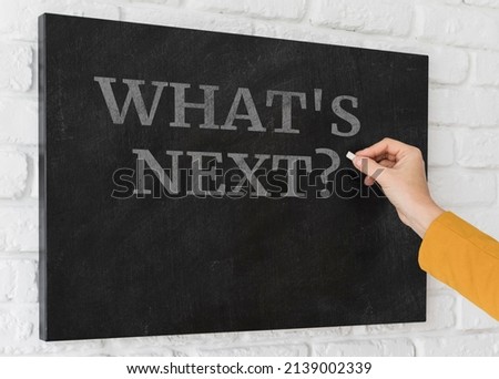 A hand writing 'What's Next?' on chalkboard.