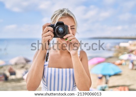 Young blonde girl smiling happy using camera at the beach.