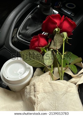A bouquet of beautiful red roses and a glass of coffee in the car