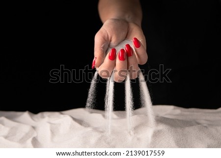 Woman with handful of white dry sand in her hands, spilling sand through fingers on black studio background. Concept of flow of life. Close up of grains of pure natural mineral quartz in female hand. Royalty-Free Stock Photo #2139017559