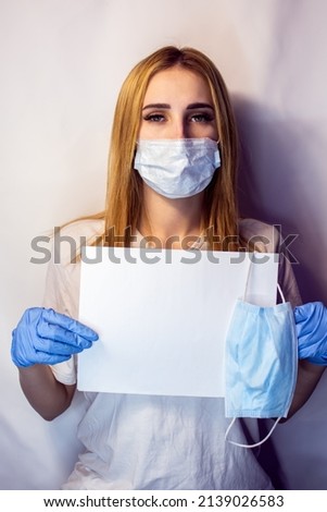A girl in a mask on her face holds a no Covid19 sign in her hands. The tablet in the hands of a girl on a white background. Blonde with a white table in her hands. No covid 19.