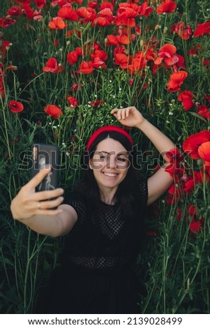 beautiful woman in black dress taking selfie at the poppies flowers field