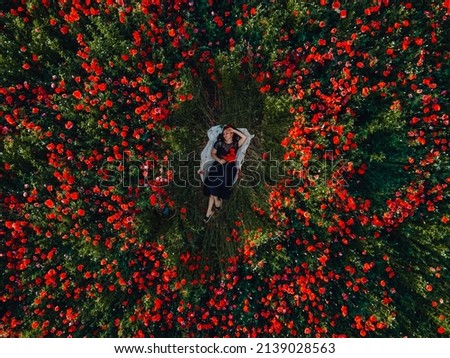 woman laying down on the middle of blooming poppies flowers field directly above