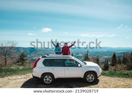 young woman sitting on the top of the suv car at mountain peak enjoying the landscape view at summer sunny day Royalty-Free Stock Photo #2139028719