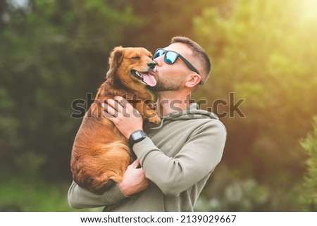 Man holding dog in his arms and kissing him outdoors. Dog and owner together. Love for pets Royalty-Free Stock Photo #2139029667