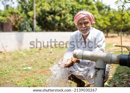 Happy Indian farmer after seeing water on borewell pipe at farmland - cocnept of happiness, poverty and water for agricultural works. Royalty-Free Stock Photo #2139030267